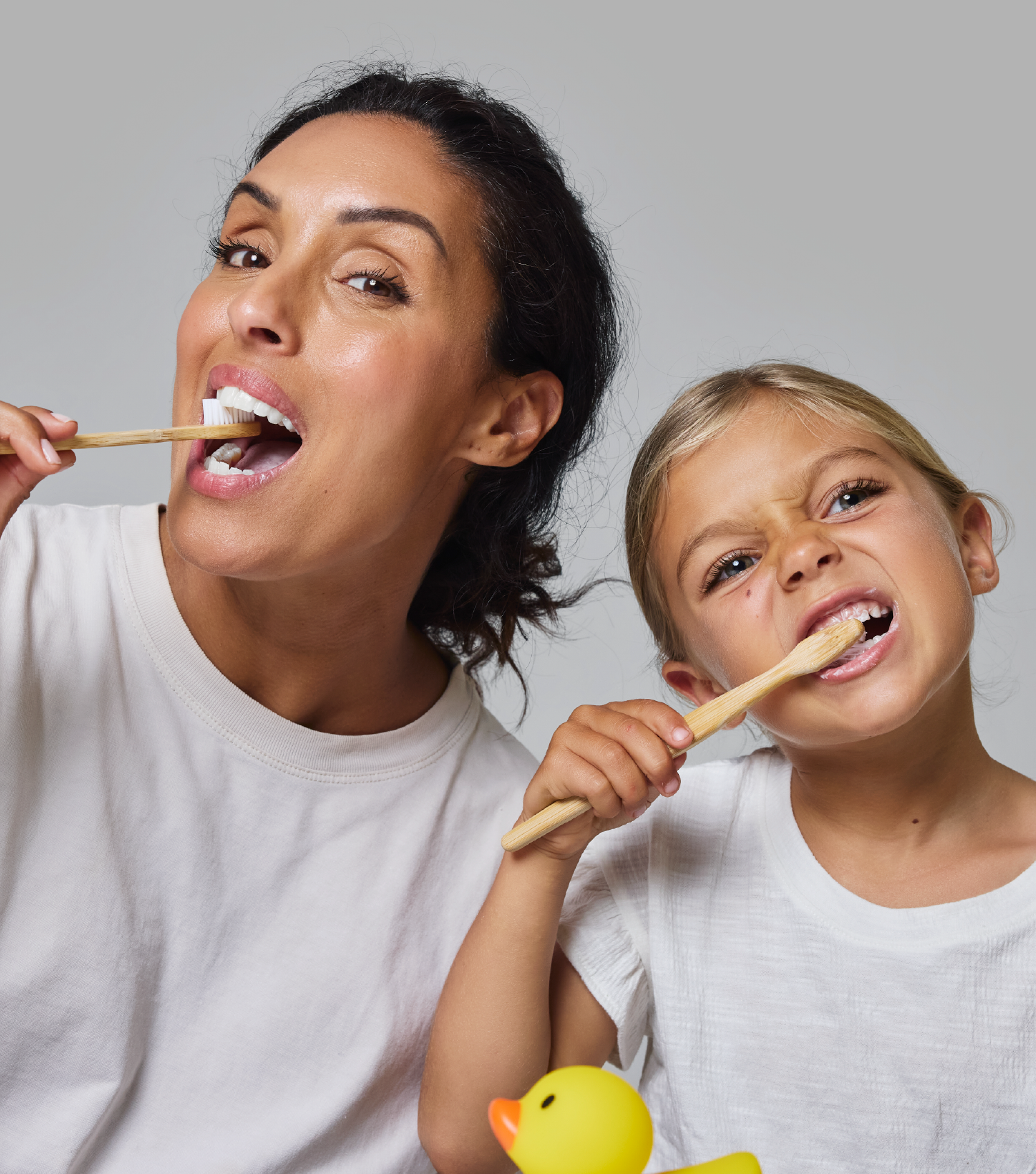 Woman and child brushing with bamboo toothbrushes, rubber duck in foreground
