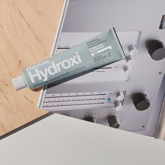 Tube of Davids Hydroxi Peppermint Whitening Toothpaste with Nano Hydroxyapatite on Dieter Rams Book and Wood Background