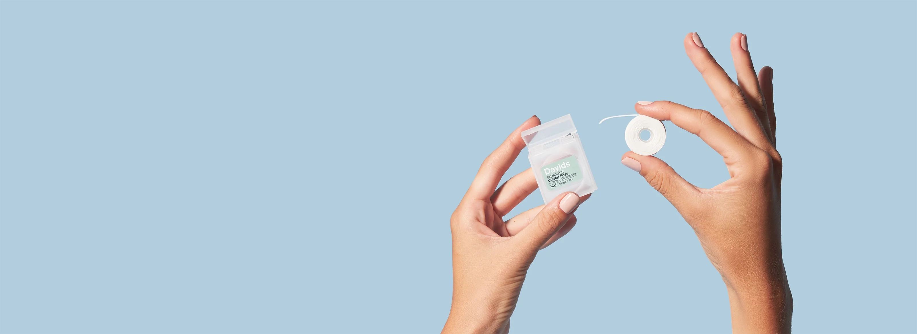 Hands holding Davids expanding dental floss and spool against a light blue background