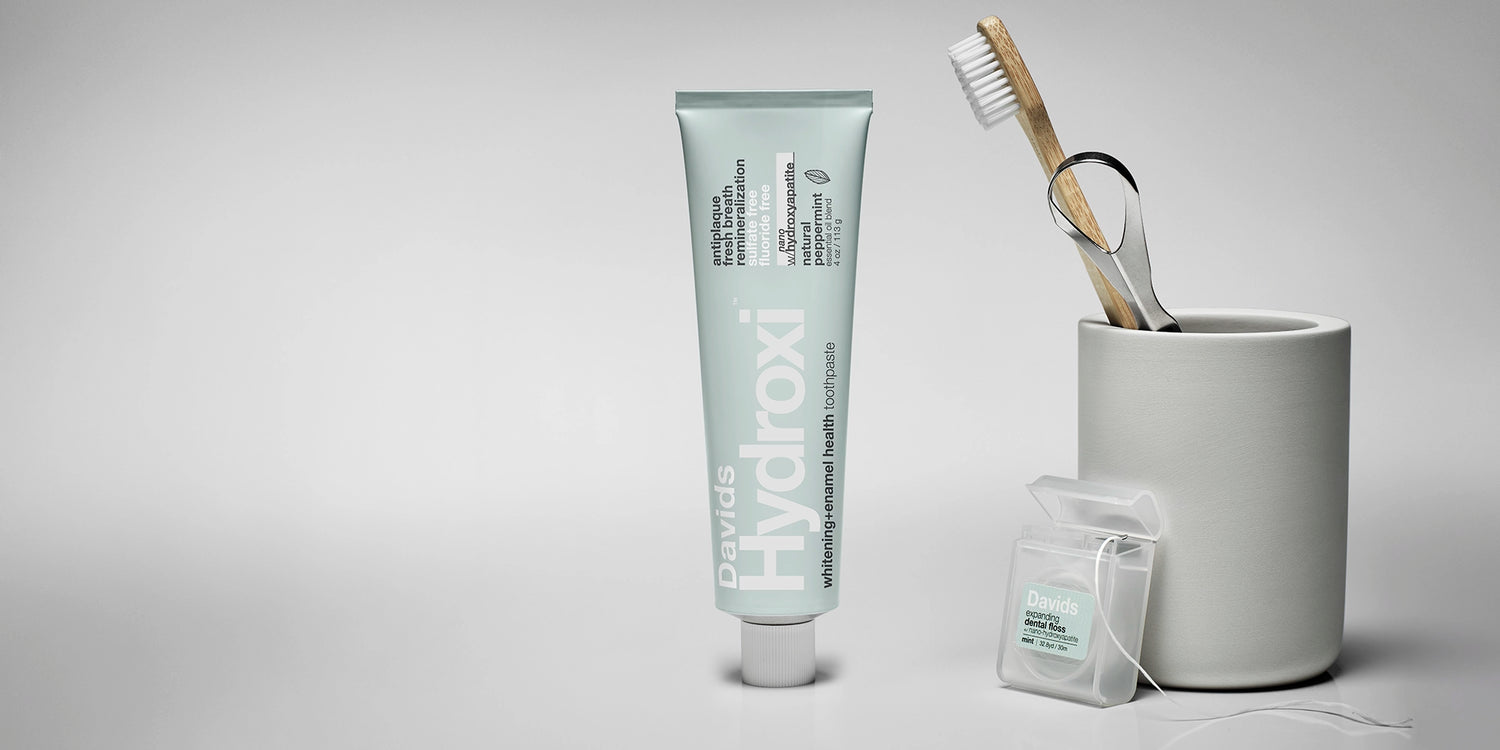 Davids nano hydroxyapatite whitening + enamel health Toothpaste tube, toothbrush, and floss on a gray background