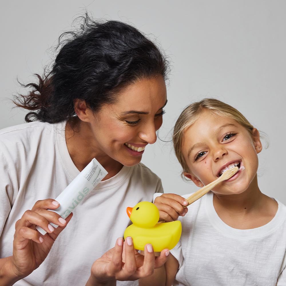 Woman holding Davids toothpaste and duck as child brushes teeth with bamboo toothbrush