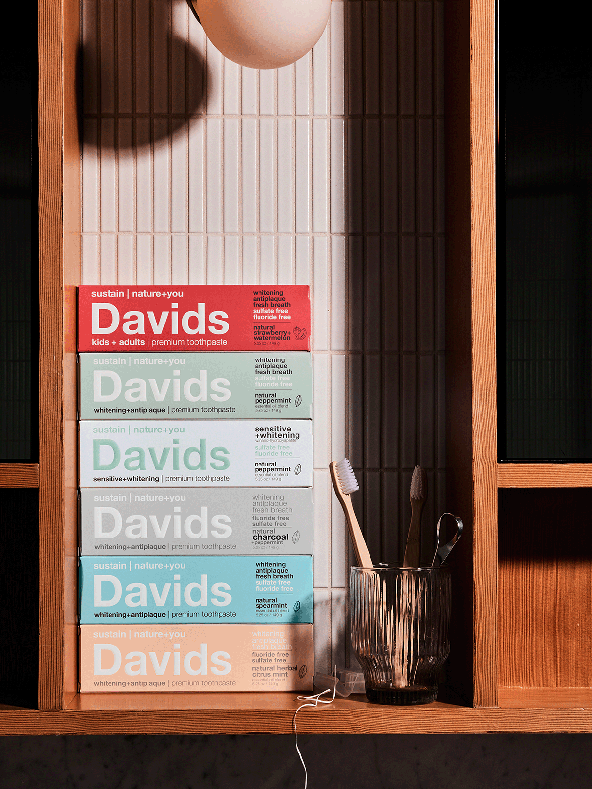 Stacked Davids toothpaste boxes with toothbrushes and tongue scraper in glass