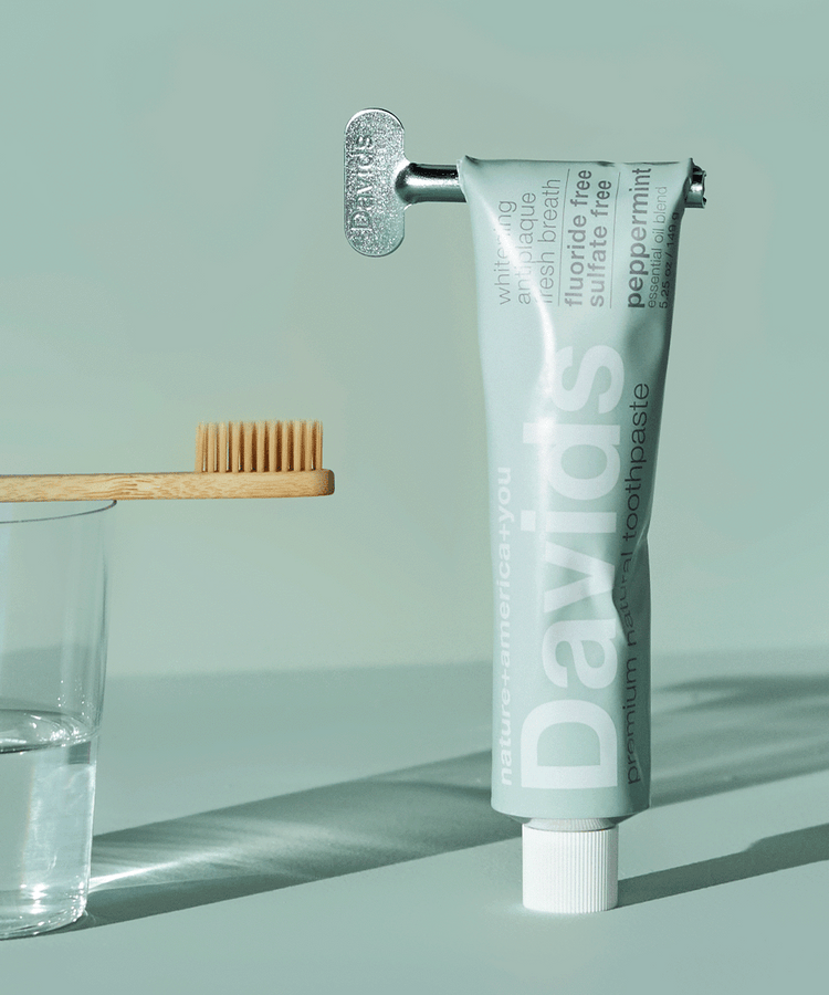 Davids toothpaste with key roller next to bamboo toothbrush on glass against mint green background