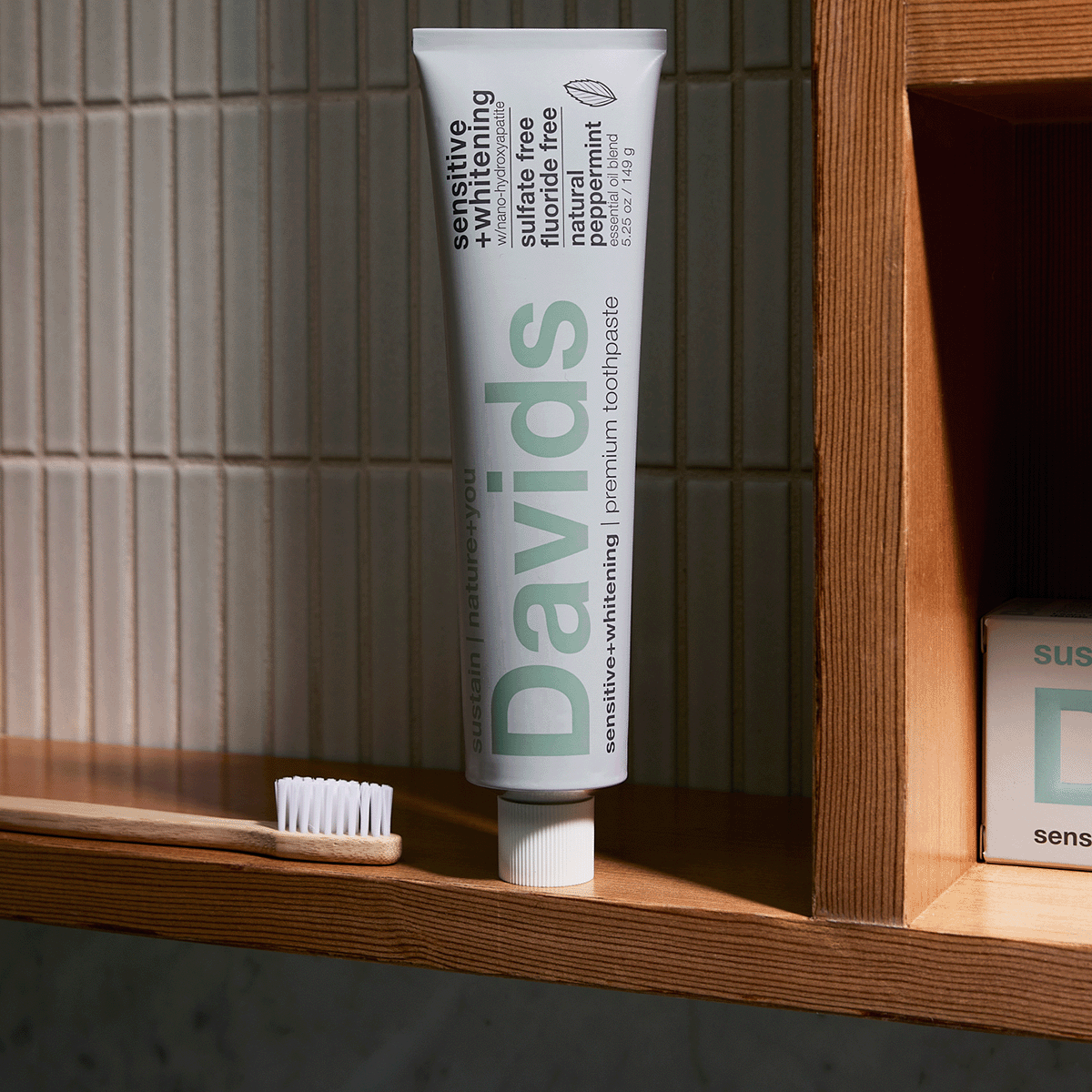 Davids sensitive + whitening toothpaste tube standing on wooden shelf with bamboo toothbrush