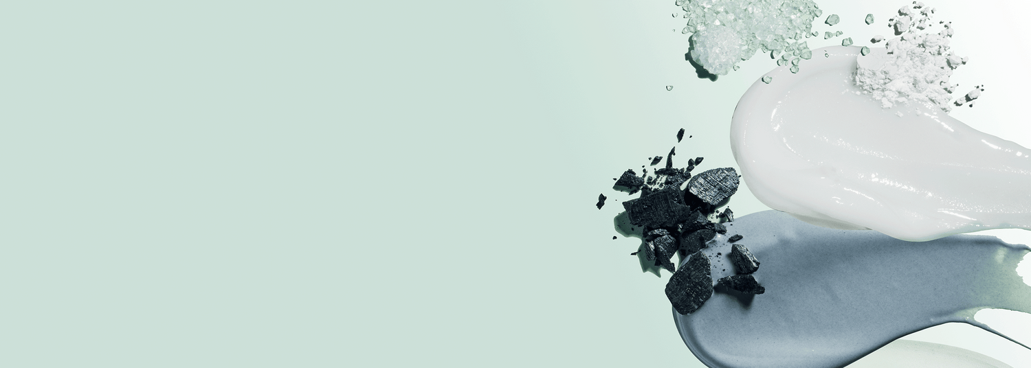 Smears of charcoal, white toothpaste, and a gray-blue paste on a pale green background