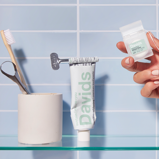 Davids toothpaste with tube key, toothbrushes, and dental floss on a glass shelf
