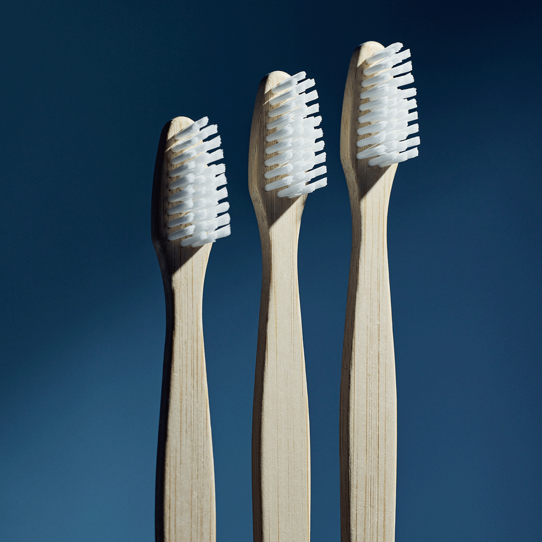 Three bamboo toothbrushes with white bristles against a dark blue background