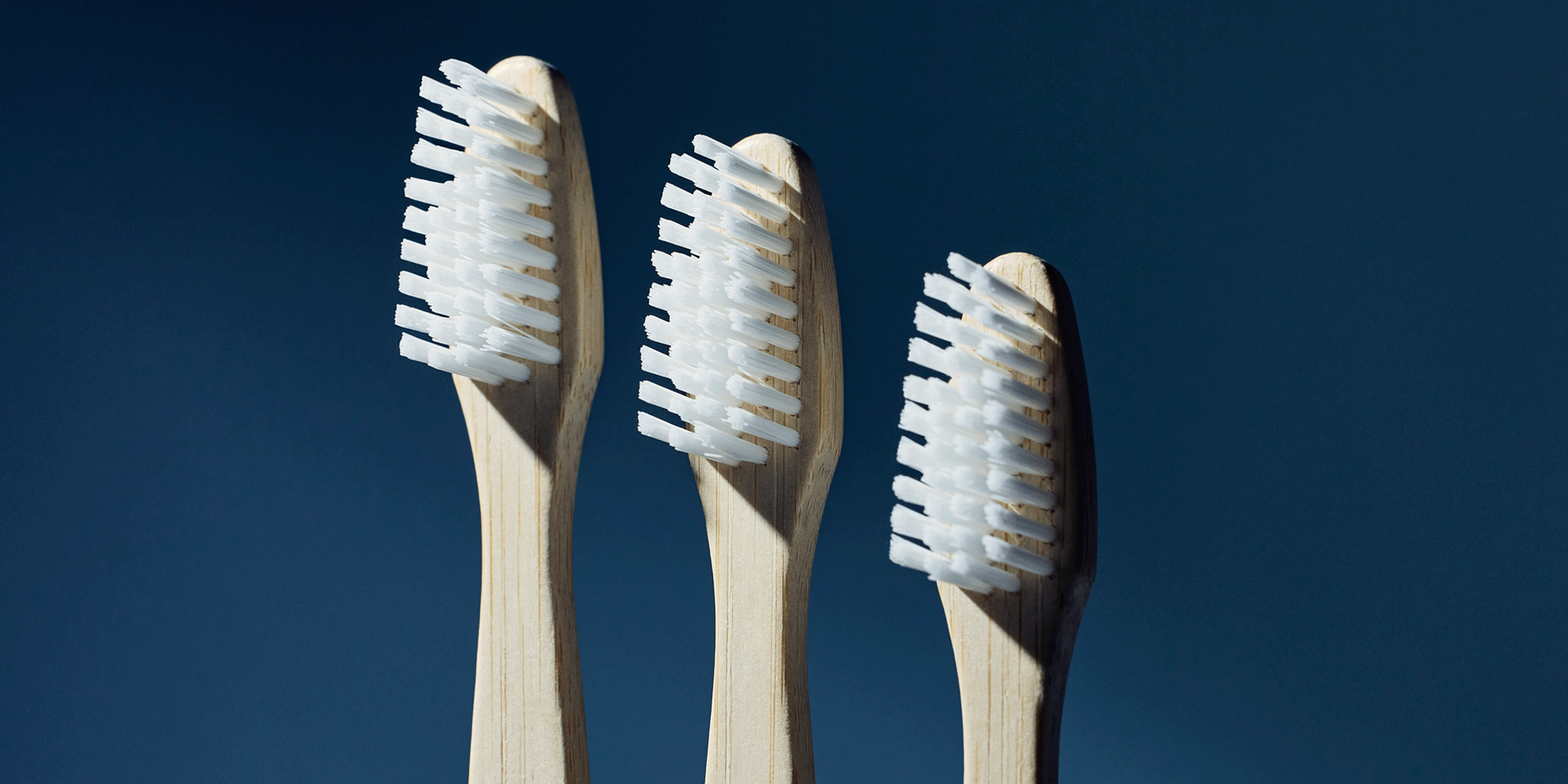 Three bamboo toothbrushes with white bristles against a dark blue background
