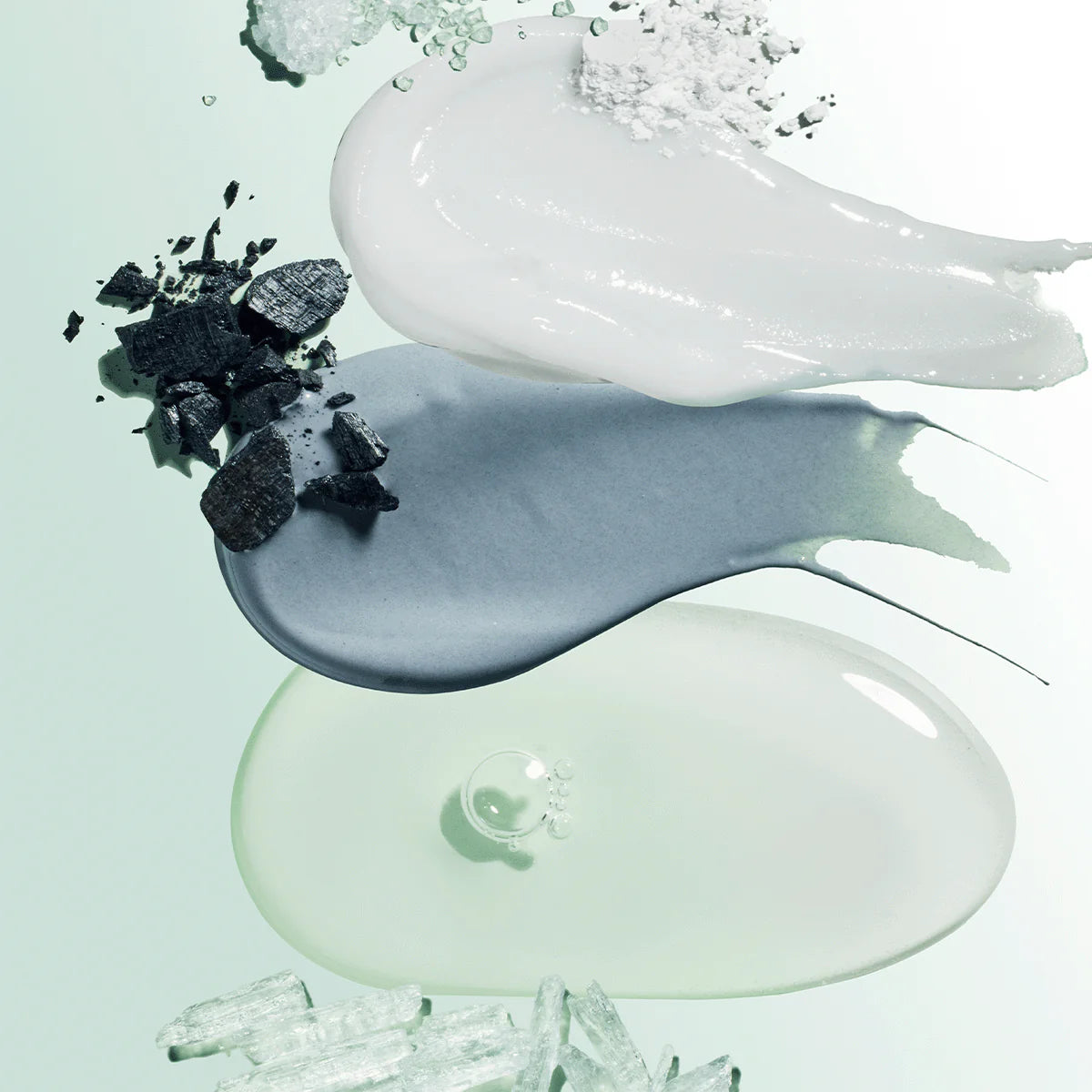 Smears of toothpaste with charcoal, powder, and crystal ingredients on a light green background