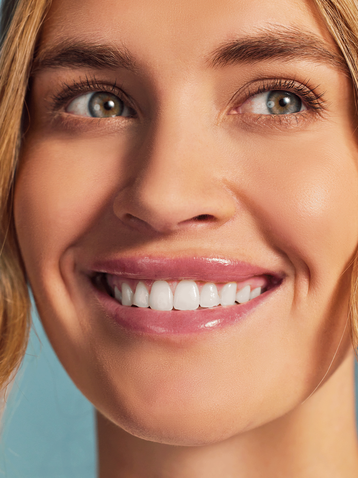 Close-up of a smiling woman with bright white teeth, clear skin, and light blue eyes looking upward